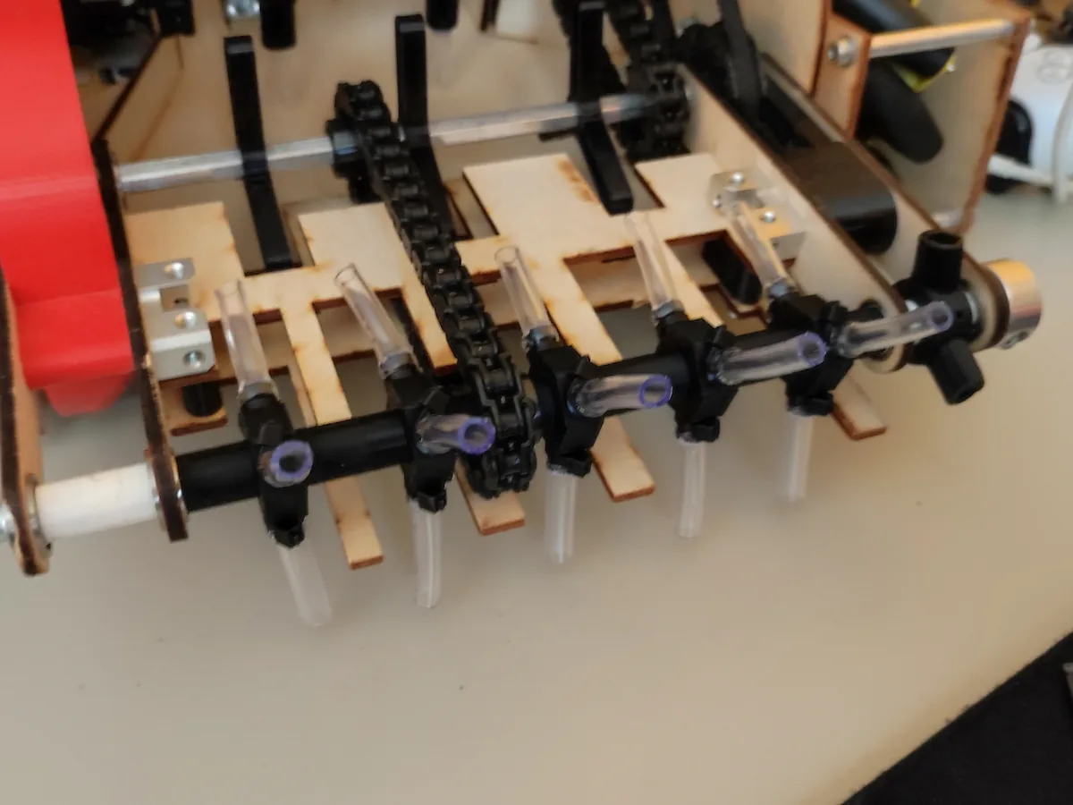 Close-up of the pivoting intake: surgical tubing brushes on a chain-driven shaft in a laser-cut plywood frame